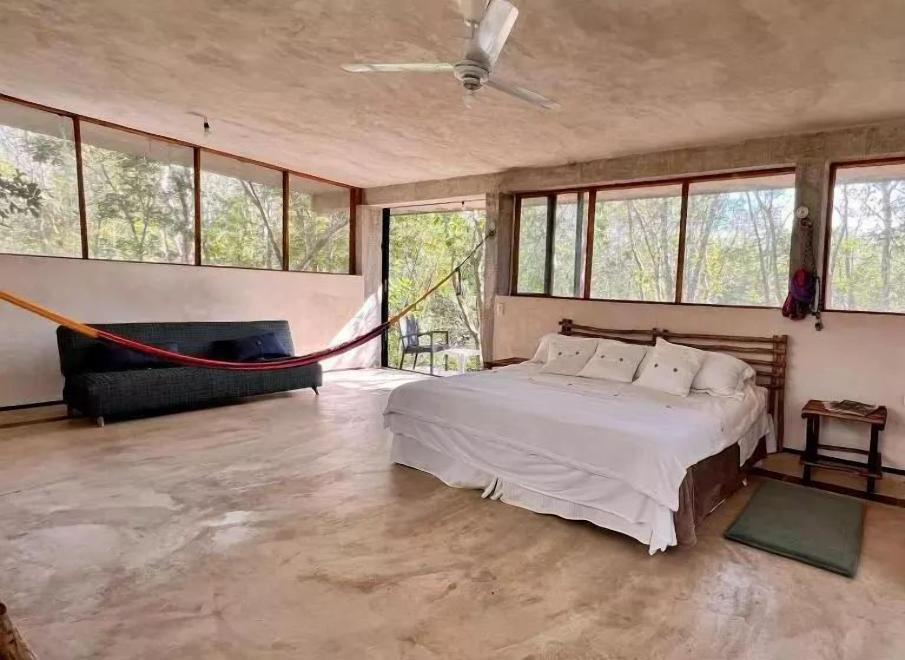 Une chambre à coucher avec un lit, un hamac et de grandes fenêtres.