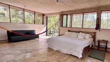 Une chambre à coucher avec un lit, un hamac et de grandes fenêtres.