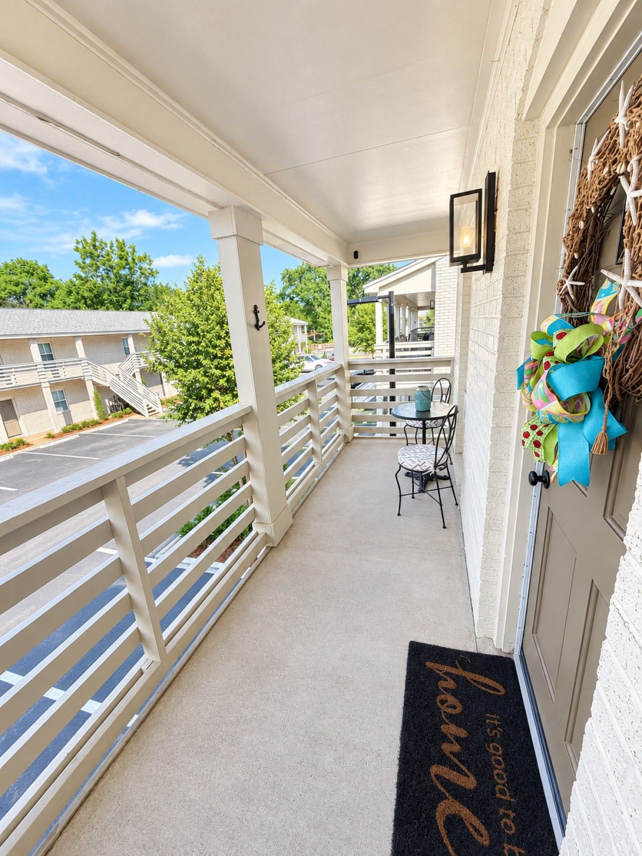 A covered outdoor area with a white railing, a small table with chairs, and a door with a doormat.