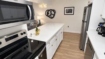 A modern kitchen with white cabinetry, a black stove, a microwave, and a refrigerator.