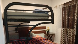 Una cama litera con una colcha escocesa, una mesita con un florero y una cortina estampada.