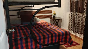 Una cama litera con una colcha escocesa, una mesita con un florero y una cortina estampada.