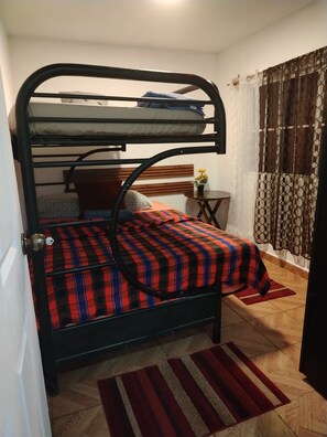 Un lit superposé avec une couvre-lit à carreaux, une petite table avec un vase et un rideau à motifs.
