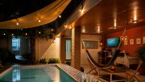 Un área de piscina con una hamaca, un televisor y una mesa con dispensador de agua.