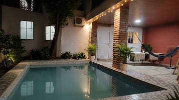 Una piscina con borde de azulejos, rodeada de plantas en macetas y una hamaca.