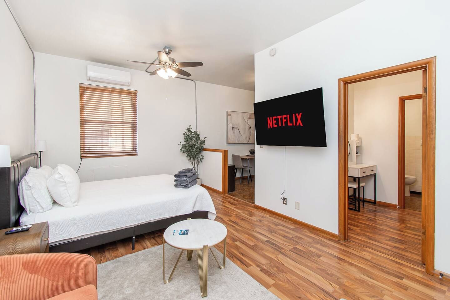 Een moderne hotelkamer met een bed, een aan de muur bevestigde televisie, een plafondventilator, een klein tafeltje en een plant.