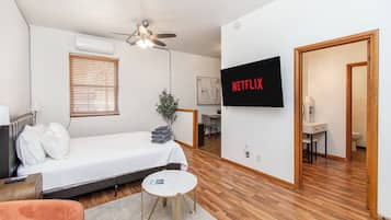 Een moderne hotelkamer met een bed, een aan de muur bevestigde televisie, een plafondventilator, een klein tafeltje en een plant.