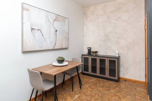 Een eetruimte met een houten tafel, een enkele stoel, een potplant en een kast met een koffiezetapparaat.