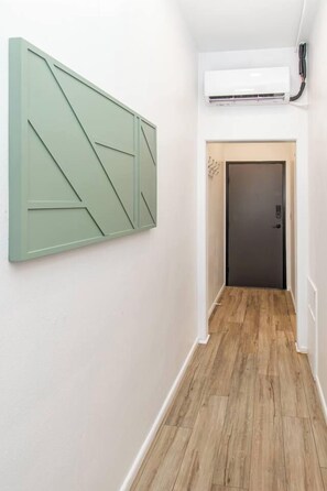 A hallway with a wooden floor, a green abstract wall panel, a door, and an air conditioning unit mounted on the wall. - 1BR I Second Story on Main #4, Walk to DT, Queen (Fargo)
