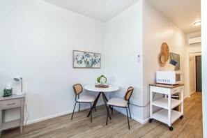 A room with a round table, two chairs, a small side table with a lamp, a framed artwork on the wall, and a white shelving unit with a microwave. - 1BR I Second Story on Main #4, Walk to DT, Queen (Fargo)