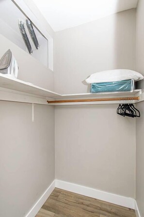 A corner room with a wooden floor, a white wall, a shelf with a white pillow, and a clothes rack. - 1BR I Second Story on Main #4, Walk to DT, Queen (Fargo)