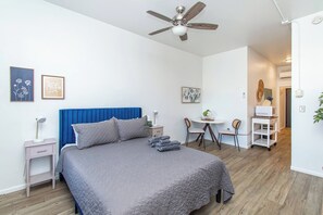 A bedroom with a bed, a desk, chairs, a ceiling fan, and artwork on the walls. - 1BR I Second Story on Main #4, Walk to DT, Queen (Fargo)