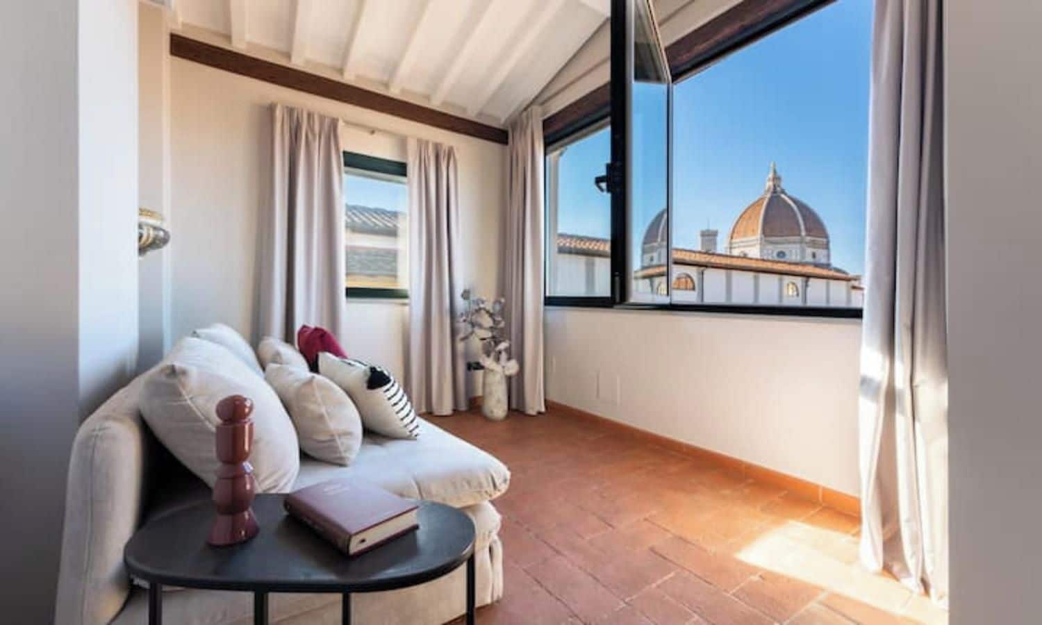 A balcony with a sofa, a small table, and a view of a dome-shaped building.