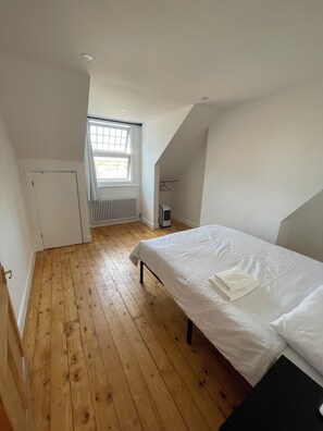 Ein Schlafzimmer mit einem Einzelbett, Holzboden, einem Heizkörper, einem Fenster und einer Tür.