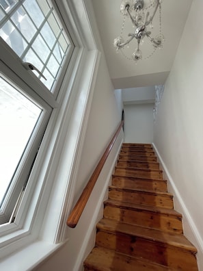 A wooden staircase with a handrail, leading to a landing with a chandelier.