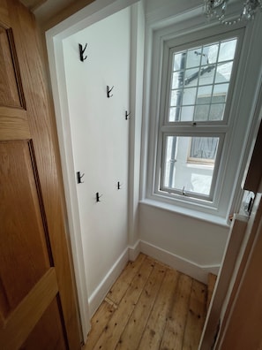 A corner room with a wooden door, a white wall with black hooks, and a window with a view of the outside.