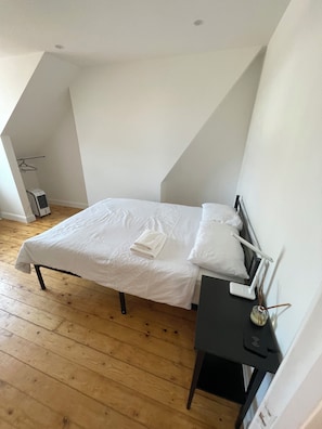 A bedroom with a bed, a bedside table, a hanging light, and a radiator.