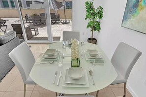 Ein Essbereich mit einem runden Tisch, gedeckt für vier Personen, weißen Stühlen und einem Blumentopf.