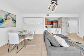 A modern living room with a gray sofa, a dining area with white chairs, and a kitchen in the background. - Midtown Miami Gem Wynwood W/ Huge Terrace Free Parking (Miami)