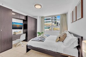 Ein modernes Schlafzimmer mit einem großen Bett, einem Schreibtisch und einem Fenster mit Blick auf Gebäude.