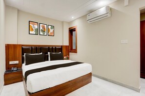 A hotel room with a bed, a nightstand, an air conditioning unit, and wall art.