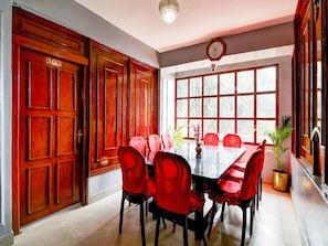 A dining area with a large wooden door marked '302', a long table with red chairs, and a clock on the wall. - Super Hotel O Ghoom Aps Homestay (Darjeeling)