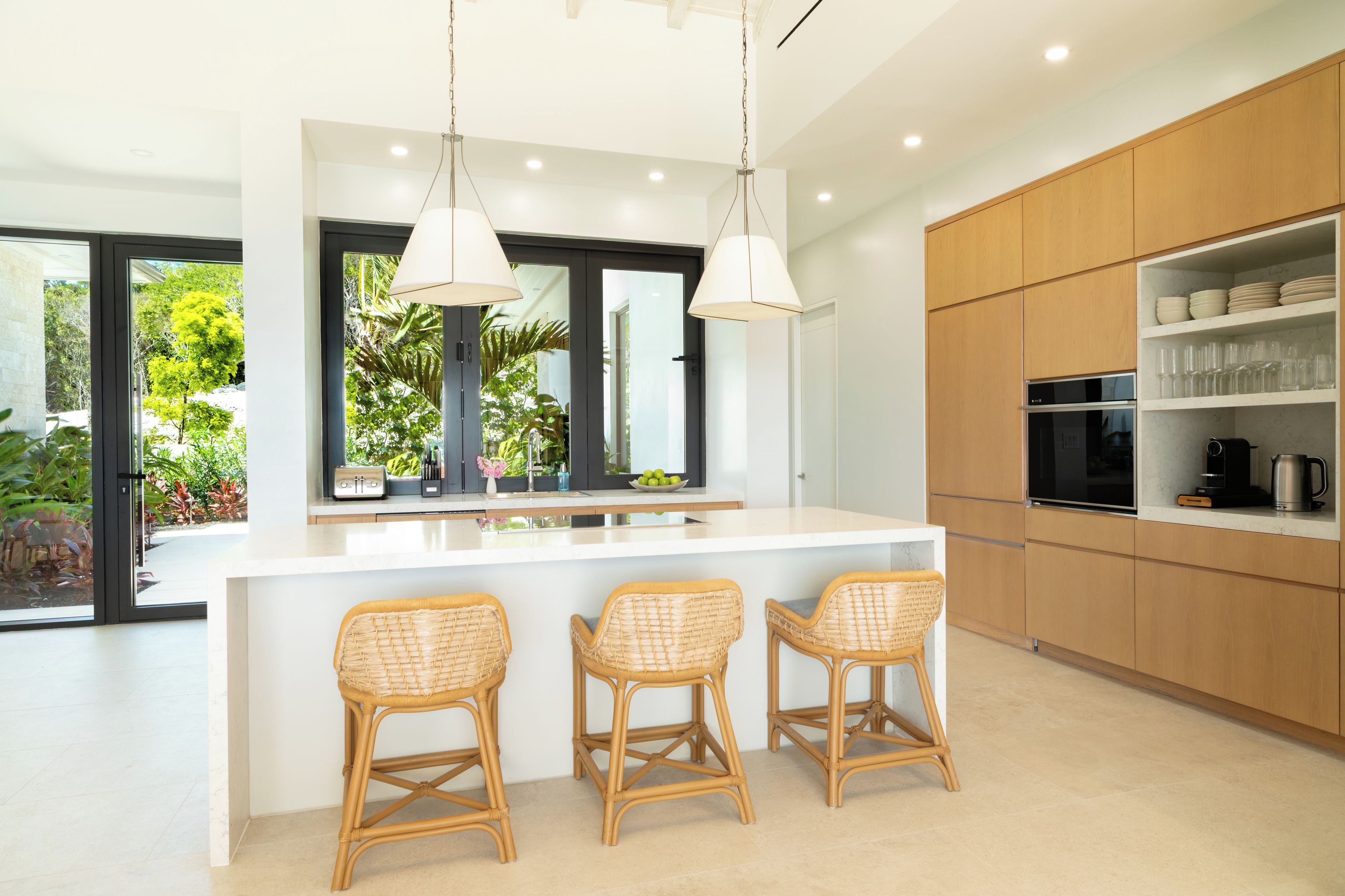 A modern kitchen with a central island, bar stools, and a view of greenery outside.