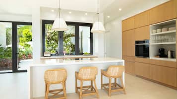 A modern kitchen with a central island, bar stools, and a view of greenery outside.