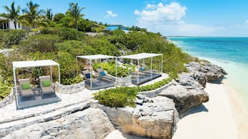 A beachside resort with outdoor seating areas, a view of the ocean, and a rocky shoreline.