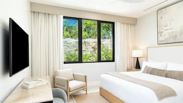 A hotel room with a bed, a chair, a desk, a TV, and a window with a view of greenery.