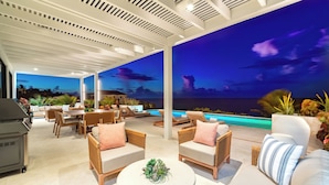 Un espacio exterior techado con piscina, sillas de descanso y una parrilla.