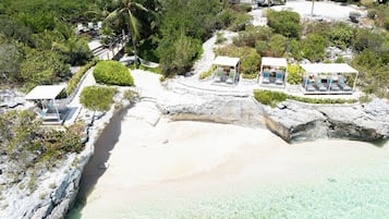 A coastal property with a rocky beach, clear waters, and a series of outdoor seating areas with umbrellas.
