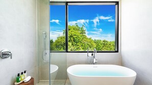 Un baño moderno con una bañera independiente, una cabina de ducha de vidrio y un ventanal con vistas a un bosque.
