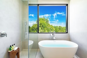A modern bathroom with a freestanding bathtub, a glass shower enclosure, and a window with a view of a forest. - Villa Blue Ocean (Blue Mountain)