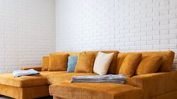 En vinkelstue med en sennepsgul sofa, et blåt pled og en væg af hvide mursten.