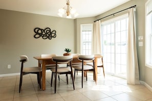 Un coin repas avec une table et des chaises en bois, un lustre et une fenêtre avec des rideaux.