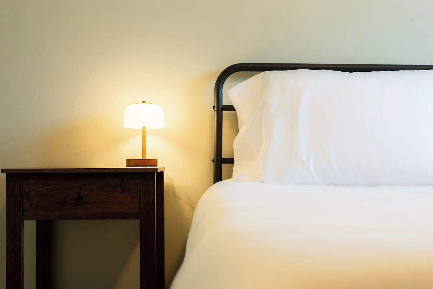 A bed with white bedding and a nightstand with a lamp.
