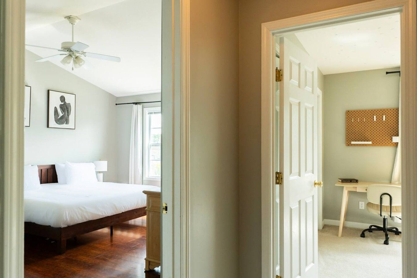 Une chambre d’hôtel comprenant un lit, un bureau avec une chaise, un ventilateur de plafond et un luminaire fixé au mur.