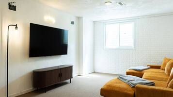 Una sala de estar moderna con un televisor de pantalla plana, un mueble de madera oscura, un ventanal grande y un sofá amarillo.