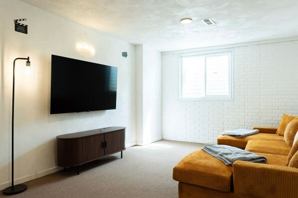 A modern living room with a flat-screen TV, a dark wooden cabinet, a large window, and a yellow sofa.