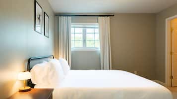 Et hotelværelse med en seng, et natbord med lampe, et vindue med gardiner og en dør.