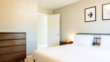 Habitación de hotel con cama, cómoda, mesita de noche y dos cuadros en la pared.