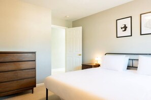 A hotel room with a bed, dresser, nightstand, and two framed pictures on the wall.