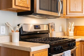 A kitchen with a stainless steel range hood, a microwave above the stove, and wooden cabinets.