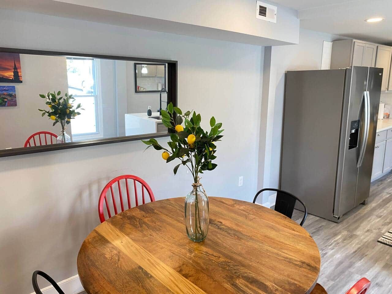 Un comedor con una mesa de madera, sillas rojas, un jarrón con flores y una cocina moderna con un refrigerador de acero inoxidable.