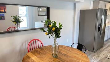 Un comedor con una mesa de madera, sillas rojas, un jarrón con flores y una cocina moderna con un refrigerador de acero inoxidable.