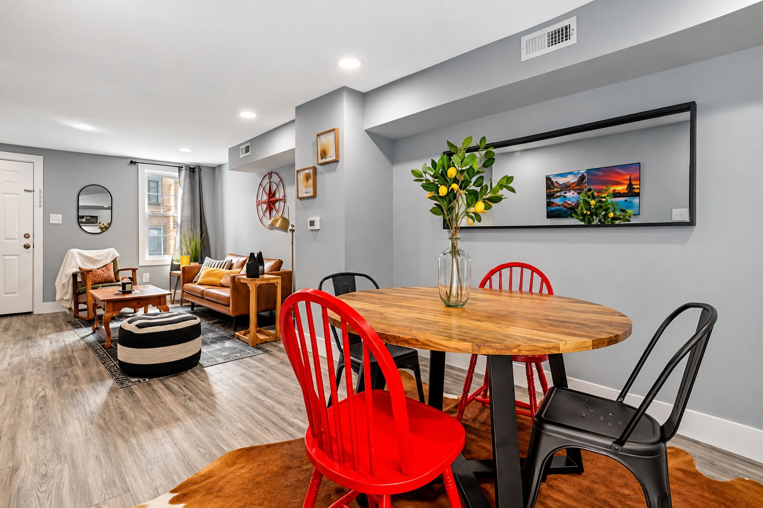 A dining area with a round wooden table, red and black chairs, and a vase with yellow flowers.