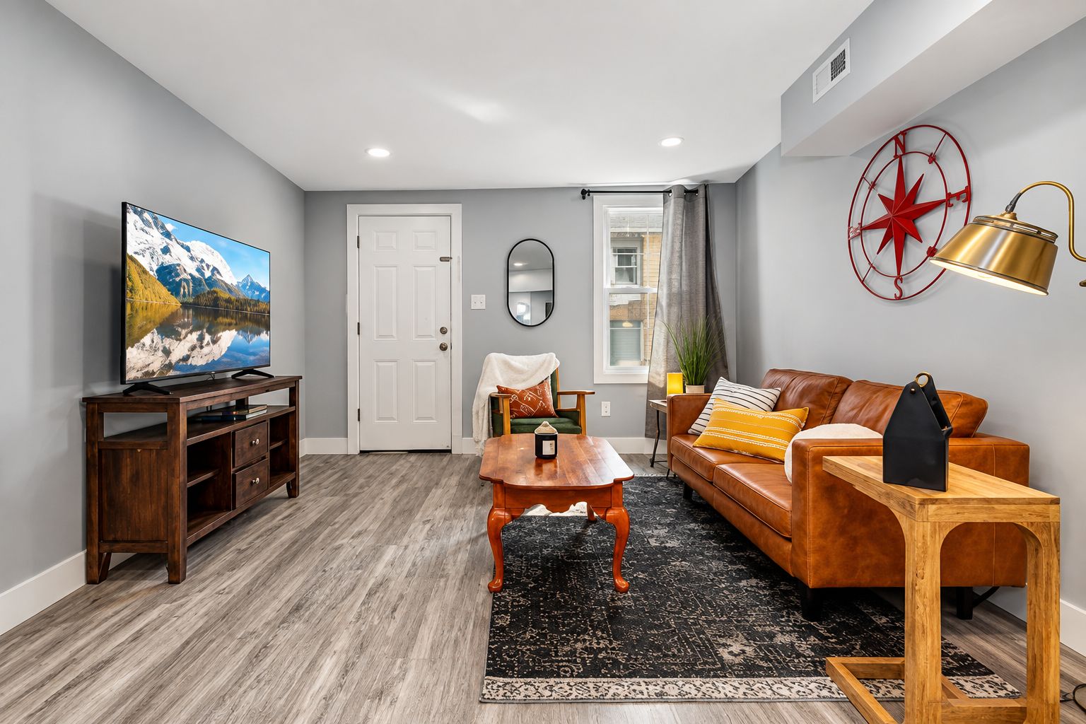 A living room with a television, a wooden coffee table, a leather sofa, and a red wall decoration.