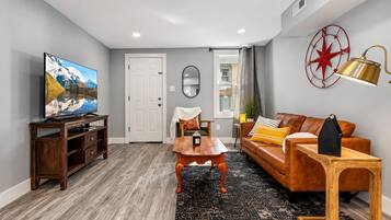 A living room with a television, a wooden coffee table, a leather sofa, and a red wall decoration.