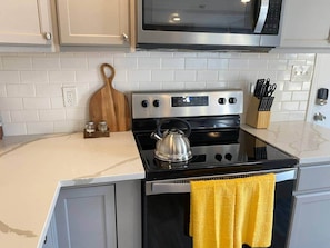A kitchen with a stove, microwave, and a kettle on the counter. - Downtown Living: Walk to Eats, Drinks & History (Frederick)